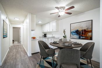 a dining area with a table and chairs and a kitchen in the background